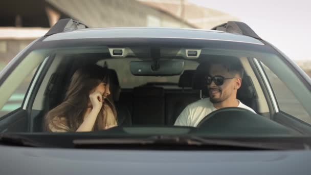 A man and a girl are sitting in a car and listening to music. They are very emotionally dancing and smiling. Theyre in the parking lot. 4K — Vídeos de Stock