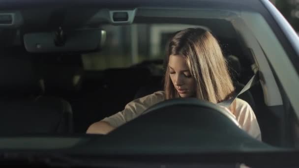 A young woman is sitting in a car in the drivers seat. She is putting on her seat belt and looking at the camera. She is smiling. 4K 50fps — Vídeo de Stock