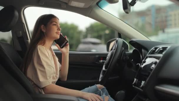 Μια νεαρή γυναίκα κάθεται στη θέση του οδηγού. Απαντάει στο τηλέφωνο και μιλάει. Έχει το χέρι της στο τιμόνι. 4K 50fps — Αρχείο Βίντεο