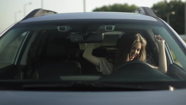 Μια ευτυχισμένη γυναίκα κάθεται στο αυτοκίνητό της στη θέση του οδηγού. Ακούει μουσική και χορεύει. Χαμογελάει. 4K — Αρχείο Βίντεο