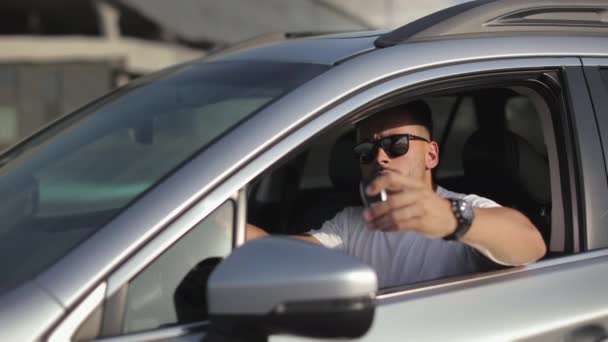 The man is sitting in the car in the drivers seat. He is looking at the camera and showing the car key. Focus on the key. Hes wearing sunglasses. 4K — Vídeo de Stock