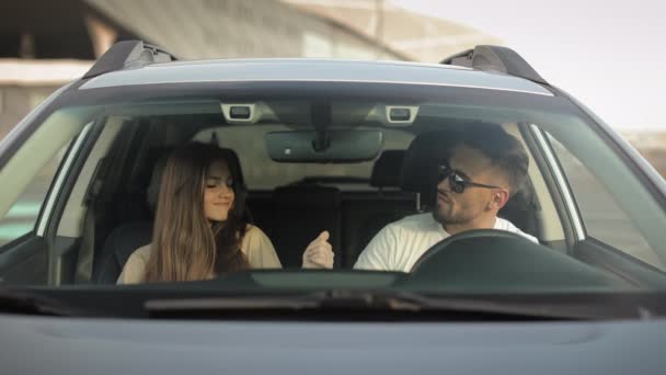 A man and a girl are sitting in a car and listening to music. They are dancing and smiling. Theyre in the parking lot. 4K — Stockvideo