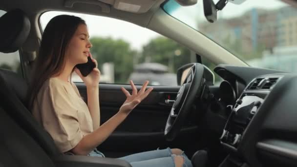 A young woman is sitting in the drivers seat. She is talking emotionally on the phone and waving. Shooting from the side seats. 4K 50fps — Vídeo de Stock