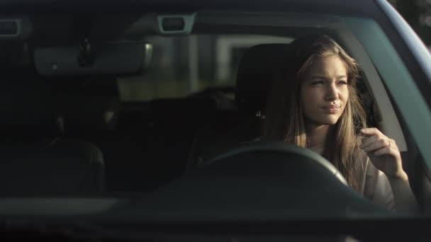 A tired woman is sitting in her car in the drivers seat. She is leaning against the door and waving her head. The sun is shining on her. 4K — Stock video