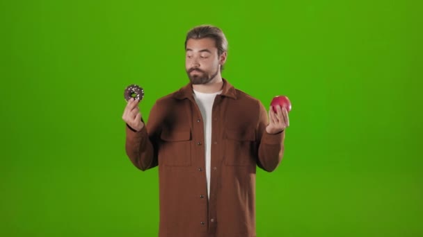 Bearded man choosing between apple and donut — Vídeo de stock