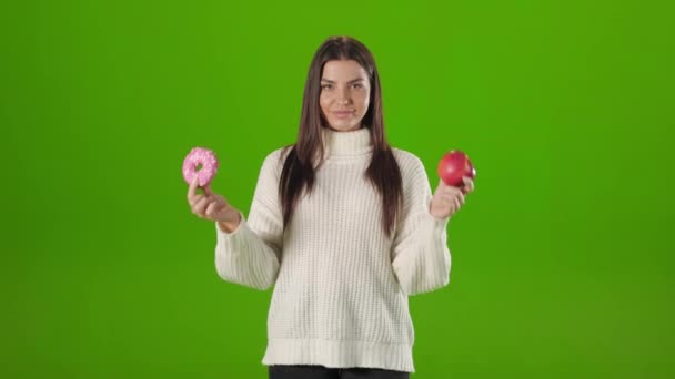 Kobieta jedząc słodkie pączki zamiast świeżego czerwonego jabłka — Wideo stockowe