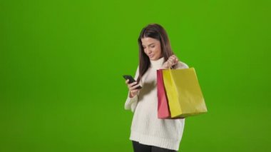 Alışveriş torbaları tutan ve akıllı telefon kullanan bir kadın.