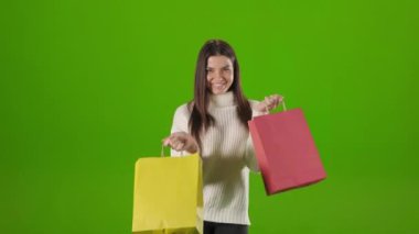 Stüdyoda renkli alışveriş torbalarıyla dans eden neşeli kadın.