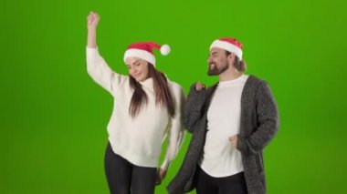 Noel Baba şapkalı neşeli adam ve kadın aktif olarak dans ediyor.