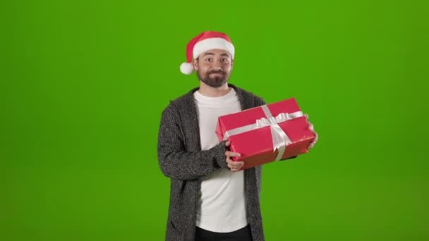 Radosny człowiek w kapeluszu Mikołaja trzęsący się kolorowy prezent w studio box — Wideo stockowe
