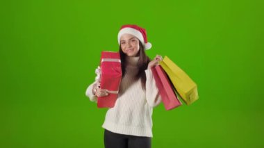 Stüdyoda alışveriş poşetleri ve Noel hediyesiyle poz veren bir kadın.