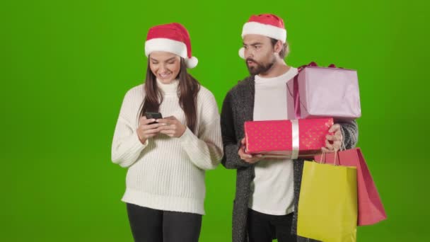 Shocked hombre sosteniendo bolsas de compras mientras que la mujer usando móvil — Vídeos de Stock