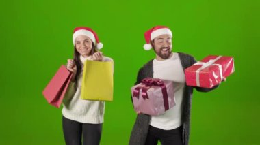 Noel Baba şapkalı neşeli çift hediyelerle ve çantalarla dans ediyor.