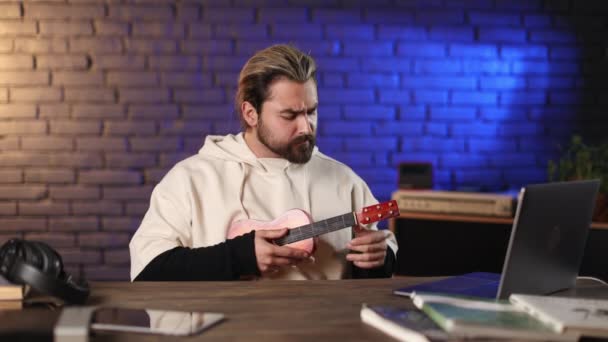 Mies käyttää kannettavaa tietokonetta opiskeluun pelata ukulele — kuvapankkivideo