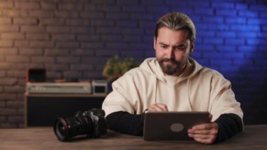 Dijital tablet ve fotoğraf makinesiyle masada oturan adam