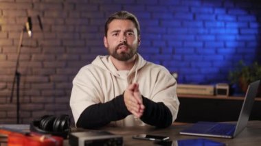 Kayıt stüdyosunda oturmuş el kol hareketi yapan ve konuşan bir adam.