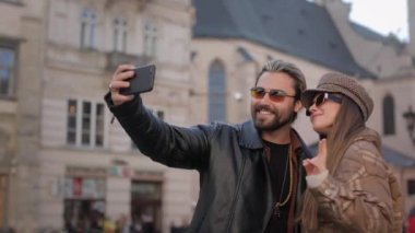 Neşeli çift sokakta selfie çekmek için akıllı telefon kullanıyor.