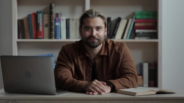 Hombre sentado en el escritorio con portátil y libro abierto — Vídeos de Stock