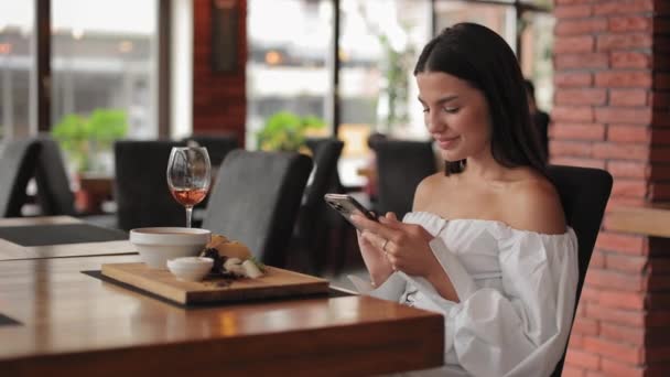 Возбужденная женщина получает хорошие новости на мобильный телефон в ресторане — стоковое видео