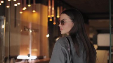 Güneş gözlüklü kadın modern otelin girişinde duruyor.