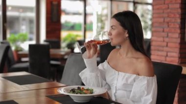 Bir bardak şarap ve salatayla restoranda oturan bir kadın.