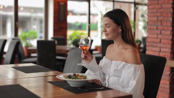 Atrakcyjna kobieta pije wino i je sałatkę w kawiarni — Wideo stockowe