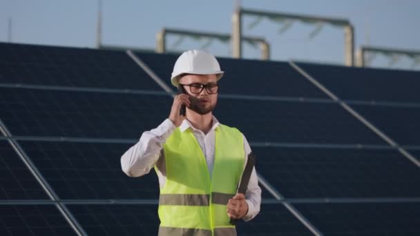 Инженер с буфером обмена говорит на мобильном телефоне на солнечной ферме. — стоковое видео