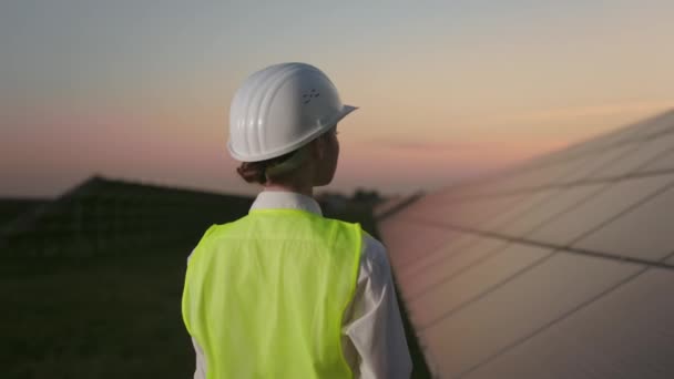 Back view of woman in helmet standing among solar farm. — Stock Video