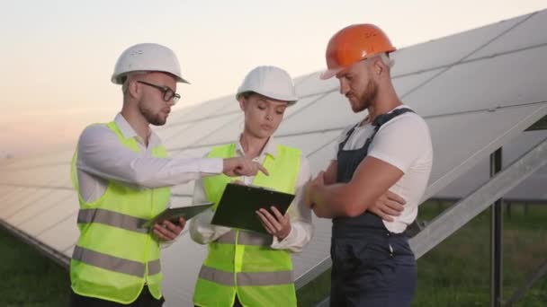 Technician talking with two inspectors among solar farm. — Stock Video