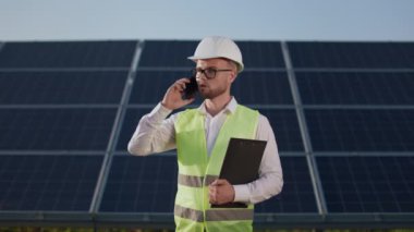 Güneş istasyonunda panosu olan bir adam cep telefonundan konuşuyor..