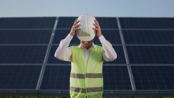 Чоловік одягає білий шолом, стоячи на сонячній станції . — стокове відео