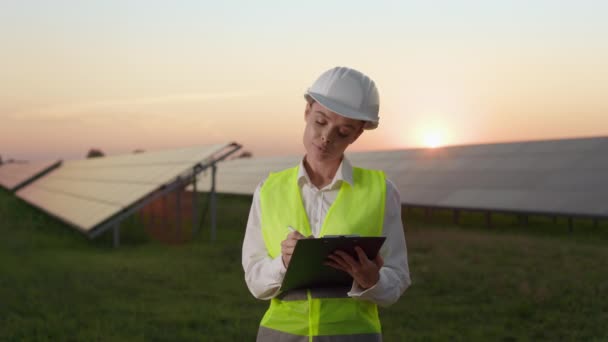 Woman writing on clipboard while working on solar farm. — Stock Video