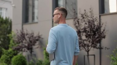 Genç bir adam iş merkezinin yakınına gidiyor. O bir dizüstü bilgisayar tutuyor. O gözlük ve bir kazak giyiyor. Etrafa bakıyor. 4k