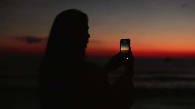 Cep telefonunda yaz günbatımını kaydeden kadın.