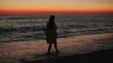 Gün batımında deniz kenarında çıplak ayakla yürüyen bir kadın.