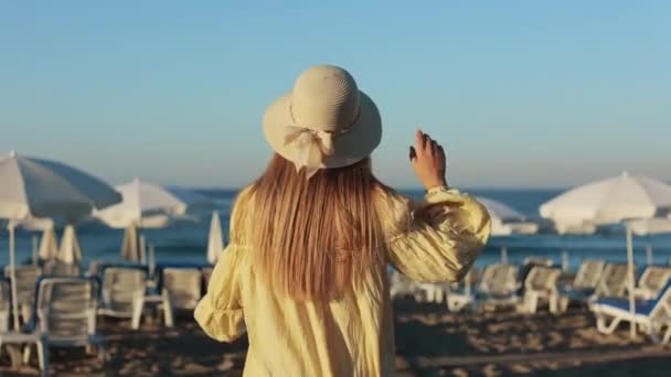 Жінка в капелюсі ходить на піщаному пляжі біля моря — стокове відео