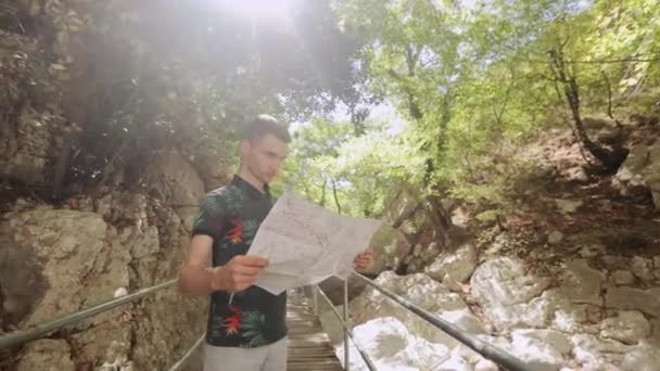 Muž s mapou stojící na mostě mezi skalnatými horami — Stock video