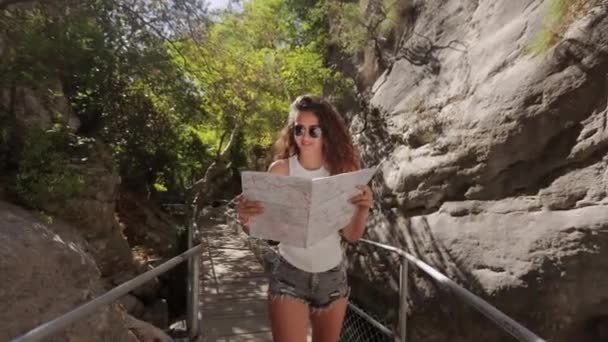 Fröhliche Frau beim Spazierengehen zwischen Felsen mit Papierkarte — Stockvideo
