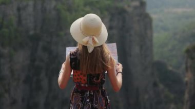 Hasır şapkalı kadın yüksek dağların tepesinde kağıt harita kullanıyor.