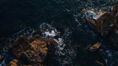 Koyu mavi dalgaların üzerindeki hava manzarası kayalara çarpıyor.