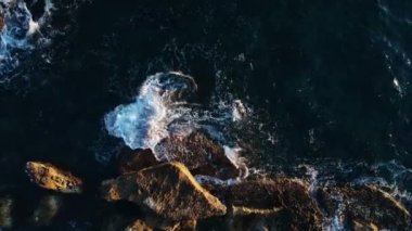 Koyu mavi dalgaların üzerindeki hava manzarası kayalara çarpıyor.