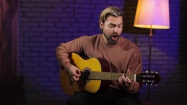 Neşeli genç adam stüdyoda ustalıkla gitar çalıyor.