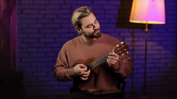 Ukulele çalan ve stüdyoda el kol hareketi yapan bir adam. — Stok video