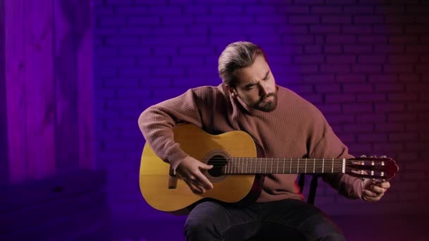 Man sitting in studio and tuning guitar before concert — Stock Video