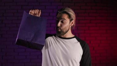 Genç adam, kağıt alışveriş torbasını parmağıyla işaret ediyor.