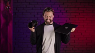 Stüdyoda kamera ve dizüstü bilgisayarlı erkek fotoğrafçı dans ediyor.