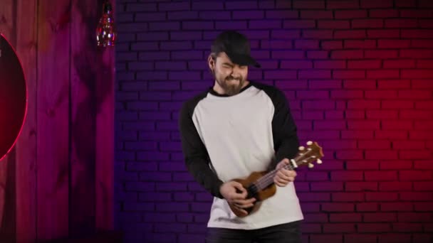 Cheerful guy dancing and singing while playing ukulele — стоковое видео