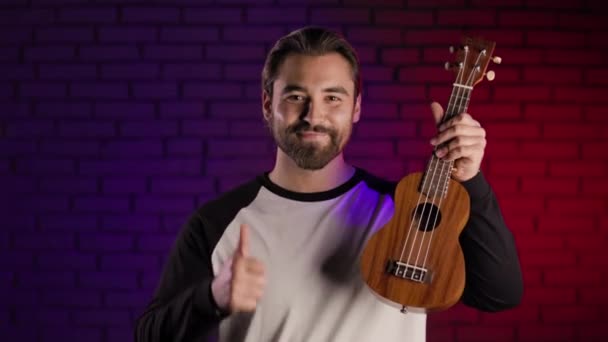 Pozytywny człowiek gestykulujący kciuk w górę i trzymający ukulele — Wideo stockowe