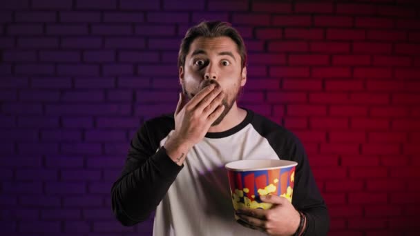 Удивленный молодой парень с корзиной попкорна смотрит кино — стоковое видео