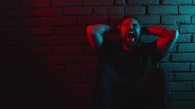 Sakallı adam stüdyoda oturuyor ve çaresizlikten bağırıyor.